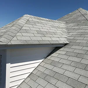 Close-up of overlapping gray asphalt-shingle rooflines under a clear blue sky, highlighting geometric patterns, texture, and bright sunlight.Close-up of overlapping gray asphalt-shingle rooflines under a clear blue sky, highlighting geometric patterns, texture, and bright sunlight.
