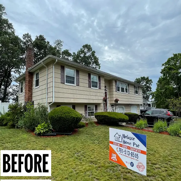 Before photo of a beige split-level suburban house with brick chimney, clipped shrubs, cloudy sky, and a landscaping company sign in the yard.